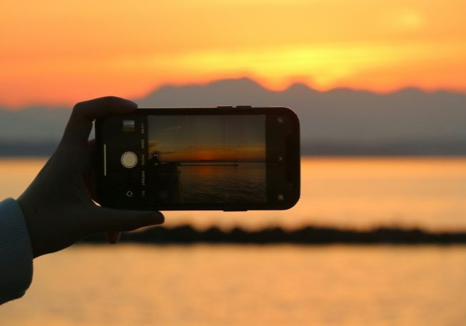 a person taking a picture of a sunset with a cell phone