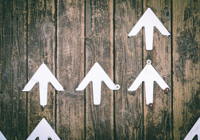 Several white arrows pointing upwards on a wooden wall